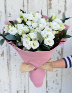 Букет от девет бели еустоми, увит в розова хартия с натурална панделка