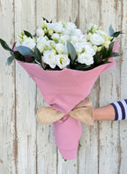 Букет от девет бели еустоми, увит в розова хартия с натурална панделка