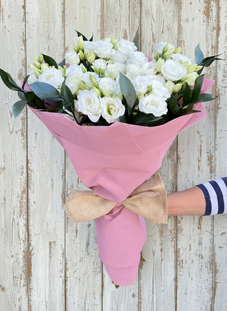 Букет от девет бели еустоми, увит в розова хартия с натурална панделка