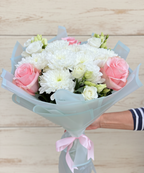 Нежен букет с розови рози, бели хризантеми и еустоми, аранжиран в пастелна опаковка и вързан с розова панделка