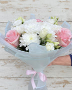 Нежен букет с розови рози, бели хризантеми и еустоми, аранжиран в пастелна опаковка и вързан с розова панделка