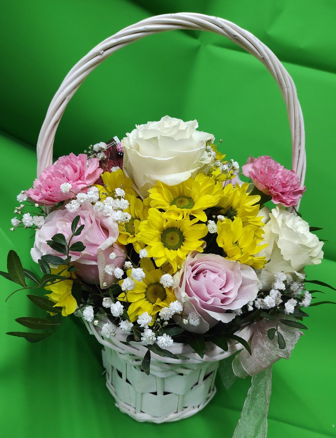 Подаръчна кошница с розови и бели рози, розови карамфили, жълти хризантеми, гипсофила и зеленина в бяла плетена кошница.