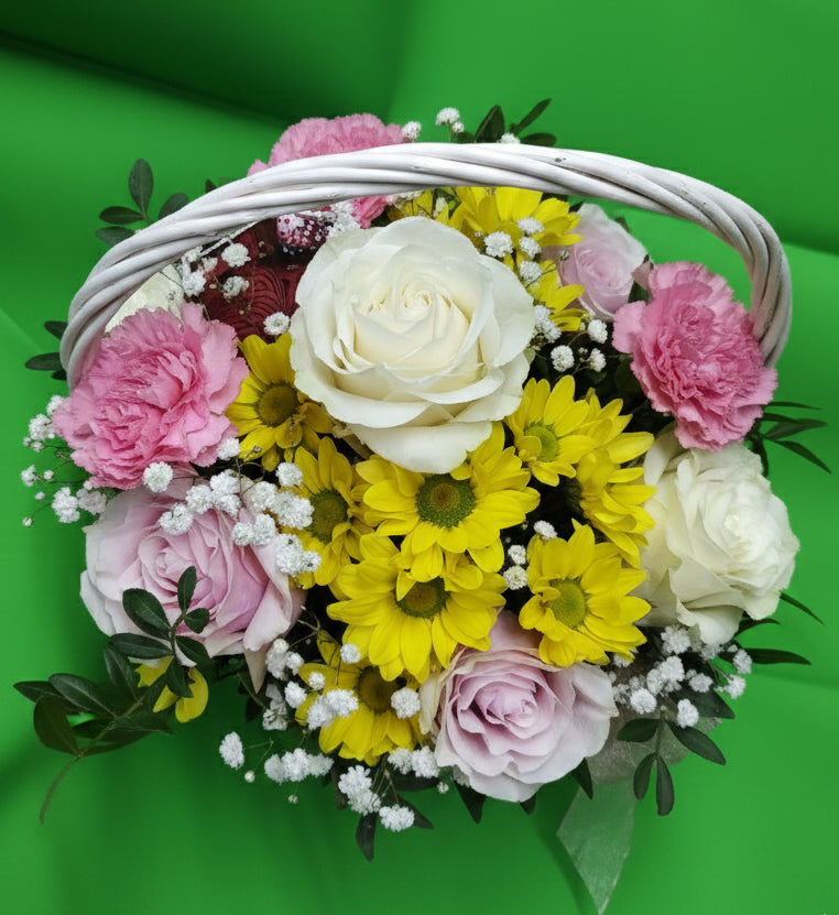 Подаръчна кошница с розови и бели рози, розови карамфили, жълти хризантеми, гипсофила и зеленина в бяла плетена кошница.